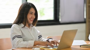 A woman is typing on a computer laptop that putting on a wooden working desk.