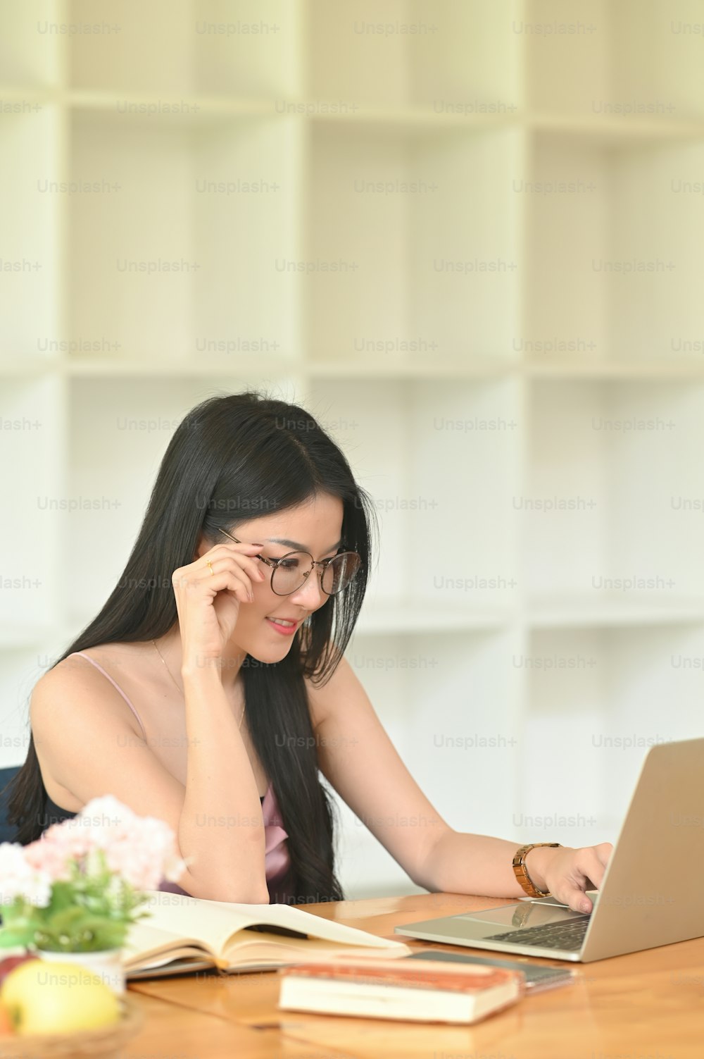 A woman with glasses is using a computer laptop while sitting at the wooden working desk.