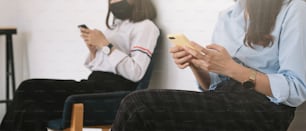 Deux jeunes femmes asiatiques discutant dans un smartphone et portant un masque à distance d’assise protègent des virus COVID-19 pour la distanciation sociale contre le risque d’infection