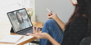 A young woman making video conference with colleagues at the wooden working desk.