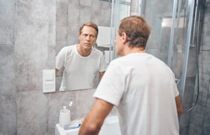 Waist-up portrait of a male looking closely at himself in the mirror on the wall