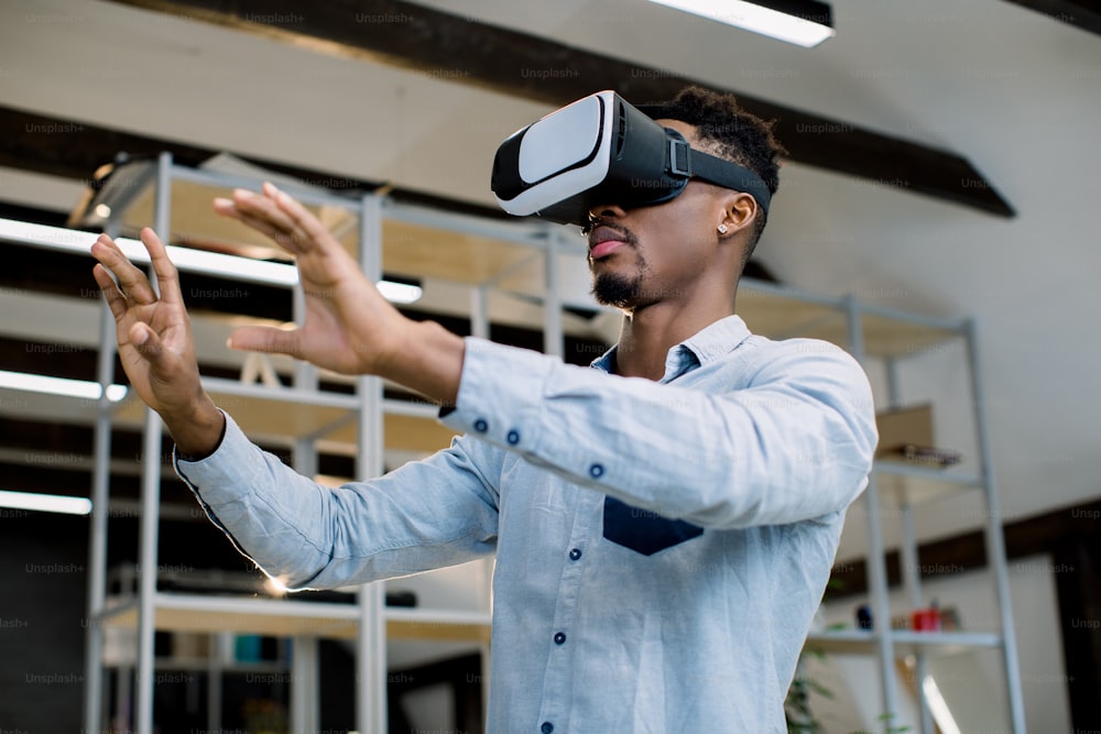 3d technology and virtual reality. Young African dark-skinned businessman dressed in casual shirt with vr goggles on head, gesturing as if interacting with something, testing video game or project.