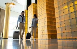 Handsome bearded man and stylish pretty woman in casual clothing walking with their luggage by a modern edifice