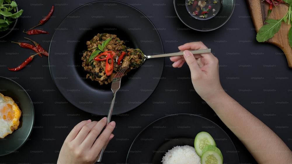 タイの伝統料理を食べる女性の上面図、黒いダイニングテーブルの上で豚ひき肉のバジル炒め(パッカプラオ)、目玉焼き、唐辛子醤