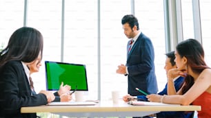 Geschäftsleute im Konferenzraum mit Greenscreen-Chroma-Key-TV oder Computer auf dem Bürotisch. Vielfältige Gruppe von Geschäftsleuten und Geschäftsfrauen in der Videokonferenz.