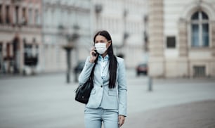 Young and elegant business woman walking on empty city street and wearing protective mask to protect herself from dangerous flu or virus. Corona virus or Covid-19 concept.