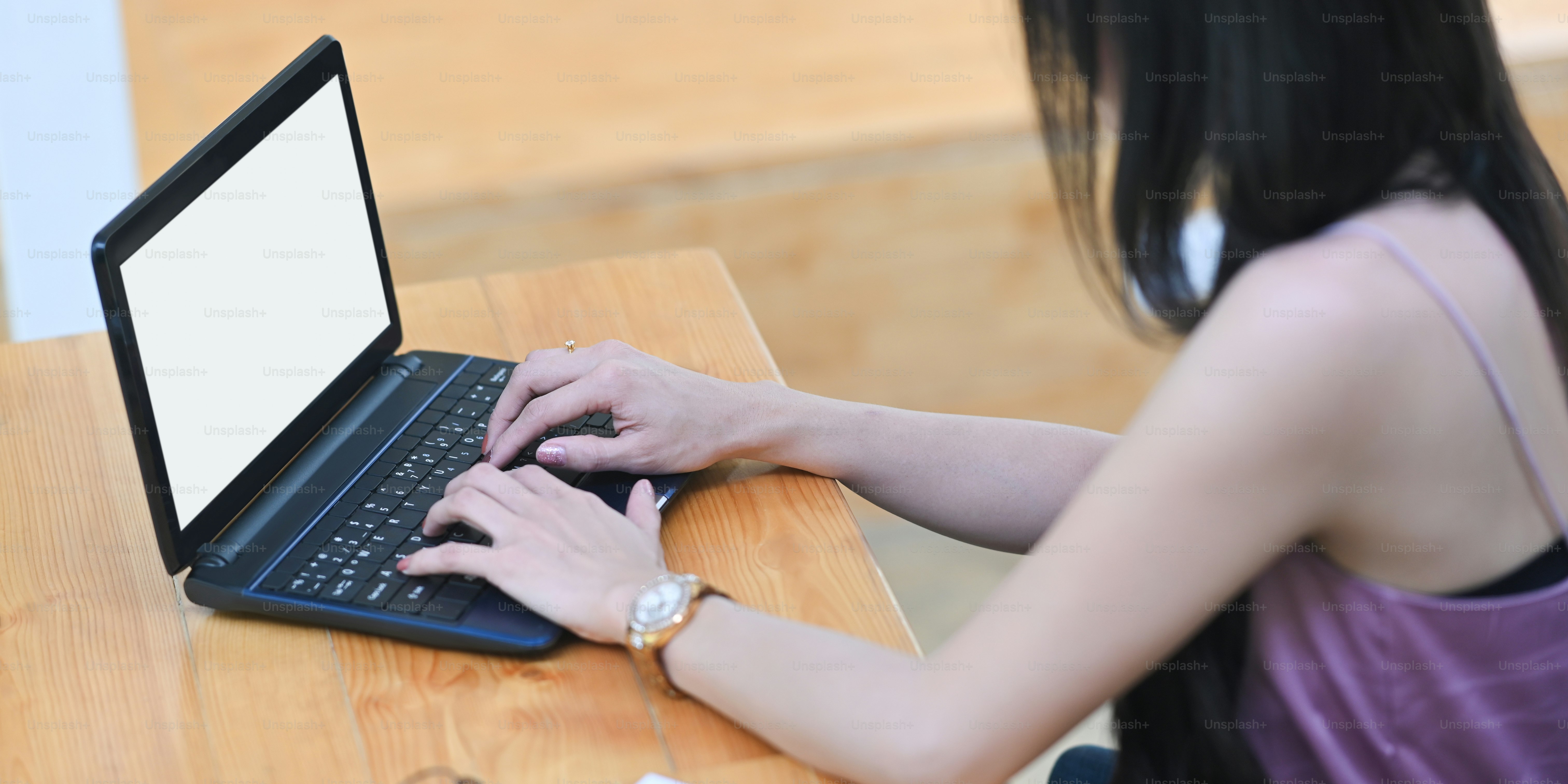 A woman is typing on a white blank screen computer laptop at the wooden working desk.