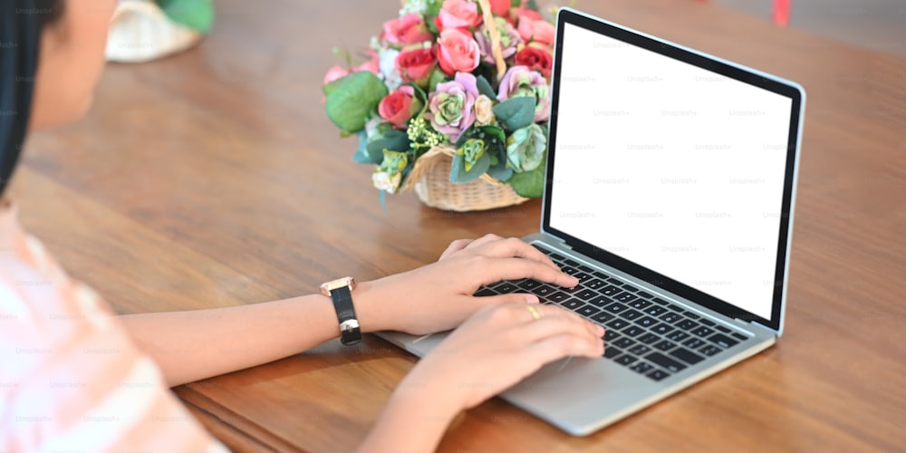 L'immagine ritagliata di una giovane donna sta digitando su un computer portatile con schermo bianco vuoto.