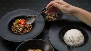 태국 전통 음식을 먹는 여성, 검은 식탁에서 바질 (Pad ka prao), 쌀, ��계란 후라이, 칠리 피쉬 소스로 다진 돼지 고기 튀김