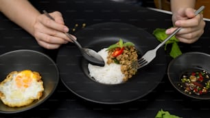 Nahaufnahme der Frau, die traditionelles thailändisches Essen isst, gebratenes Schweinehackfleisch mit Basilikum (Pad ka prao), Spiegelei und Chili-Fischsauce im thailändischen Restaurant