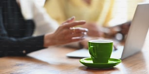 Coffee cup with a small dish is putting on a meeting table among business people as background.