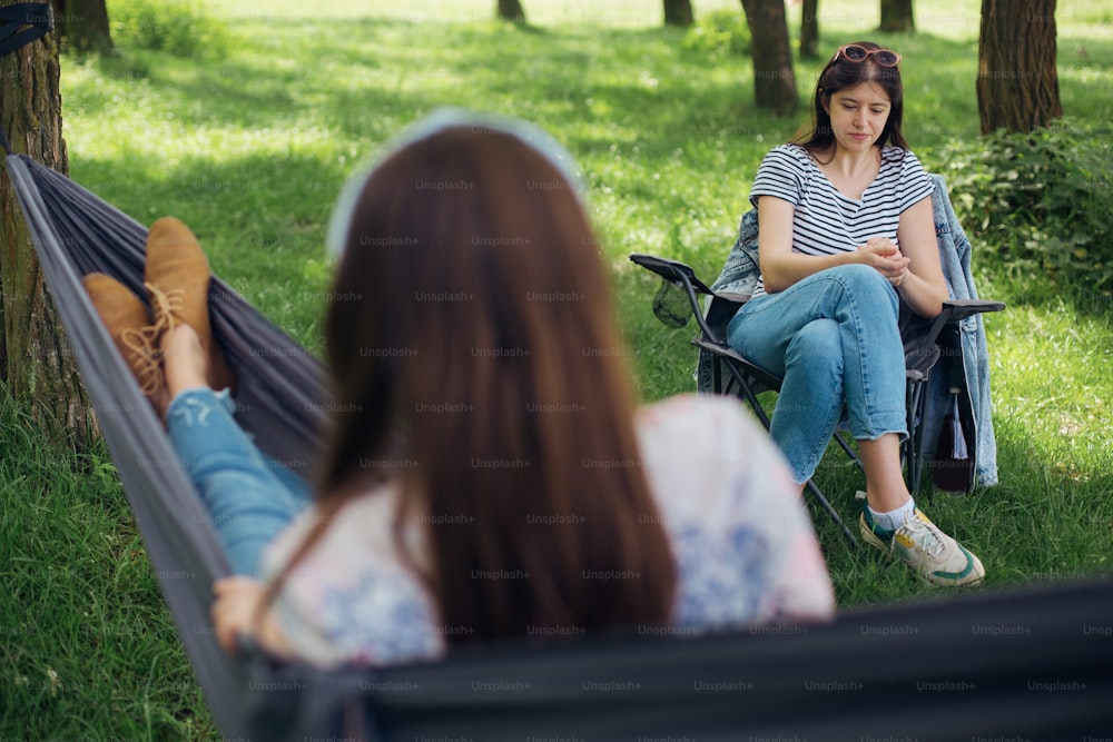 Small group of young woman enjoying conversation at picnic with social distance in summer park. Leisure activity together in new normal, safety gatherings. Social distancing
