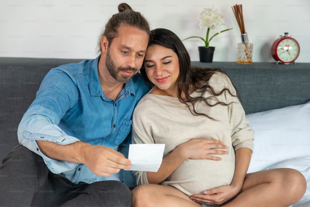 Happy Caucasian pregnant woman looking ultrasound baby picture together with her husband
