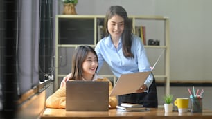 Due donne stanno lavorando insieme con un computer portatile alla scrivania di legno.