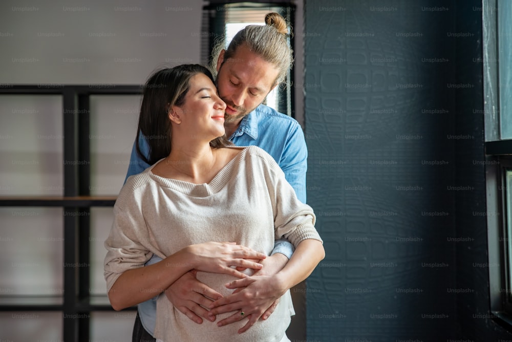 Smiling Caucasian man hug his pregnant wife from behind and strokes her tummy.
