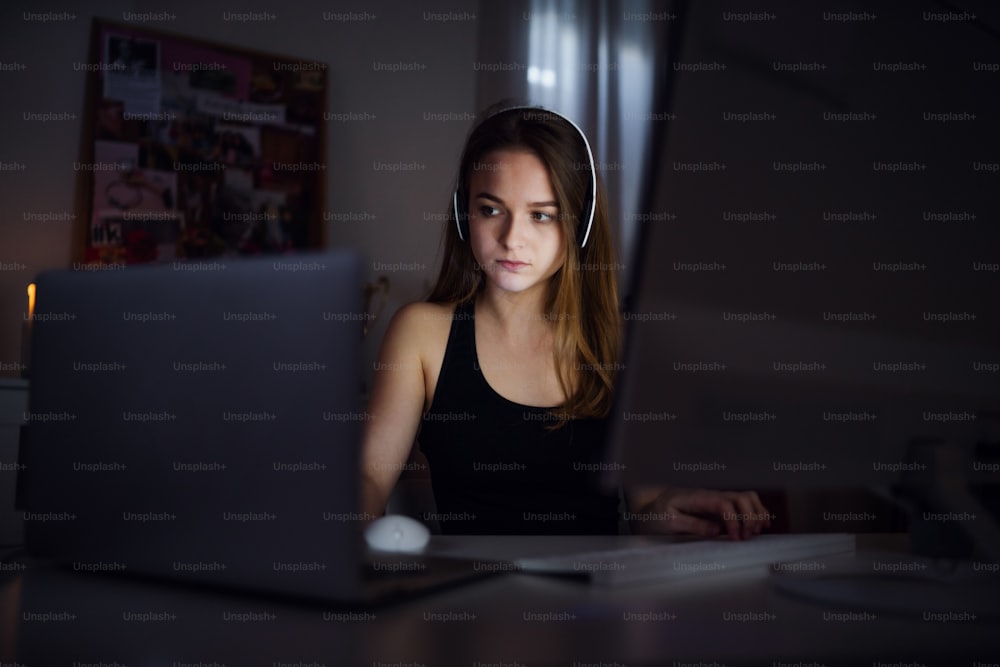 헤드폰과 컴퓨터가 실내에 앉아 있는 지루한 어린 소녀의 전면 모습, 온라인 채팅 개념.