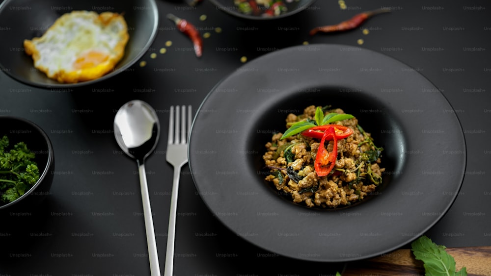 Thai traditional food, Stir fried minced pork with basil (Pad ka prao), fried egg and chili fish sauce serving on black ceramic plates in Thai restaurant