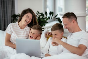 Família jovem assistindo filme no lap top. Pais bonitos com crianças desfrutando em casa.