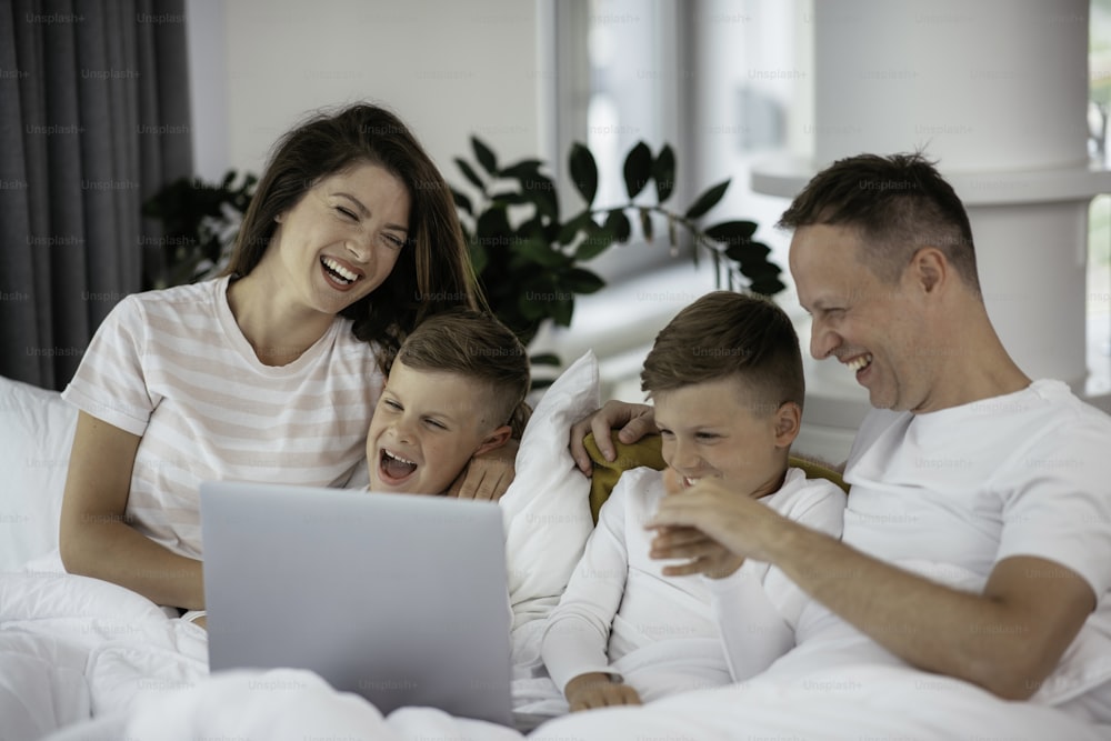 Jeune famille regardant un film sur le dessus de l’ordinateur portable. Beaux parents avec des enfants profitant à la maison.