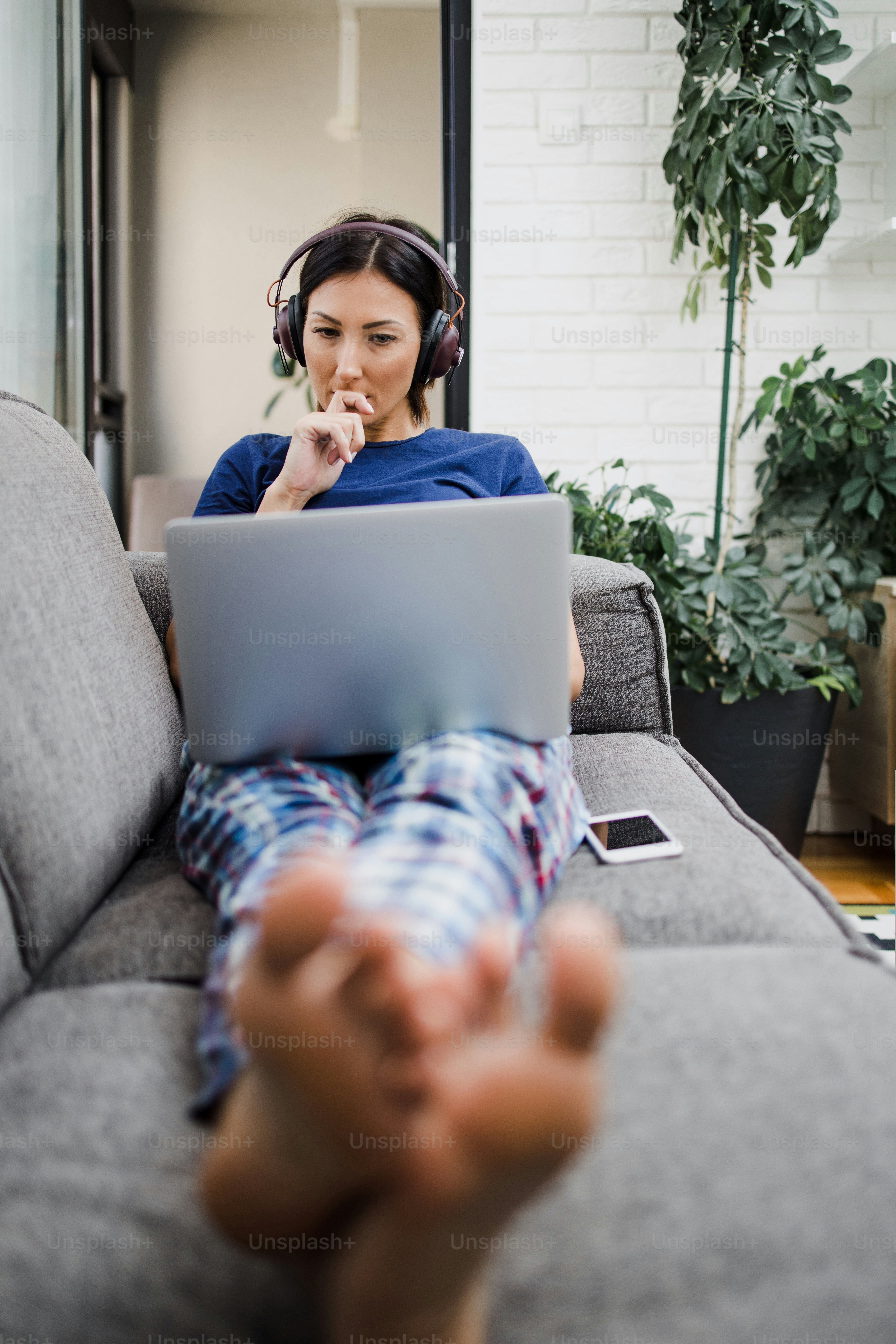 Young adult woman lying on sofa in her living room and using laptop computer for web surfing and social media communication and chat