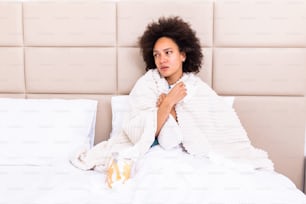 Kranke junge afrikanische Frau, die sich kalt fühlt, sitzt mit Decke bedeckt auf dem Bett, krankes schwarzes Mädchen zittert eiskalt Erwärmung zu Hause mit Plaid umwickelt, kein Zentralheizungsproblem, Fiebertemperatur Grippe-Konzept