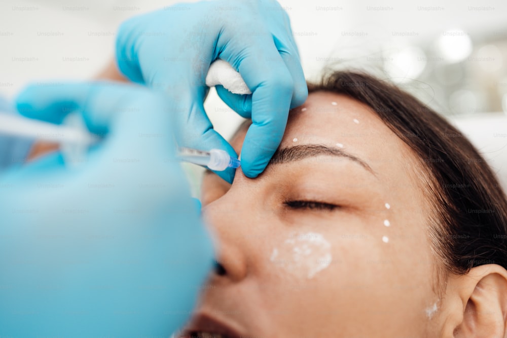 Attractive blond woman is getting a rejuvenating facial injections at beauty clinic. The expert beautician is filling female wrinkles by botulinum.