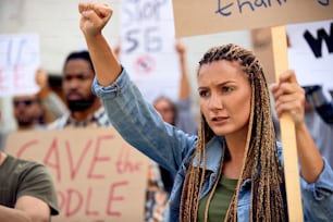 Young Caucasian woman with raised fist protesting with group of activists on city streets.