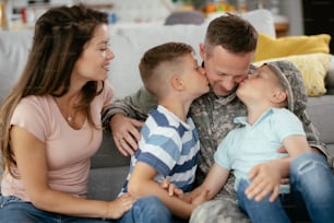 Glücklicher Soldat, der mit seiner Familie auf der Couch sitzt. Soldat und seine Frau genießen zu Hause mit Kindern.