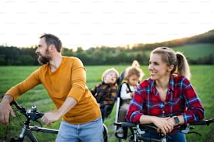 Famille avec deux jeunes enfants en voyage à vélo dans la nature, s’amuser.