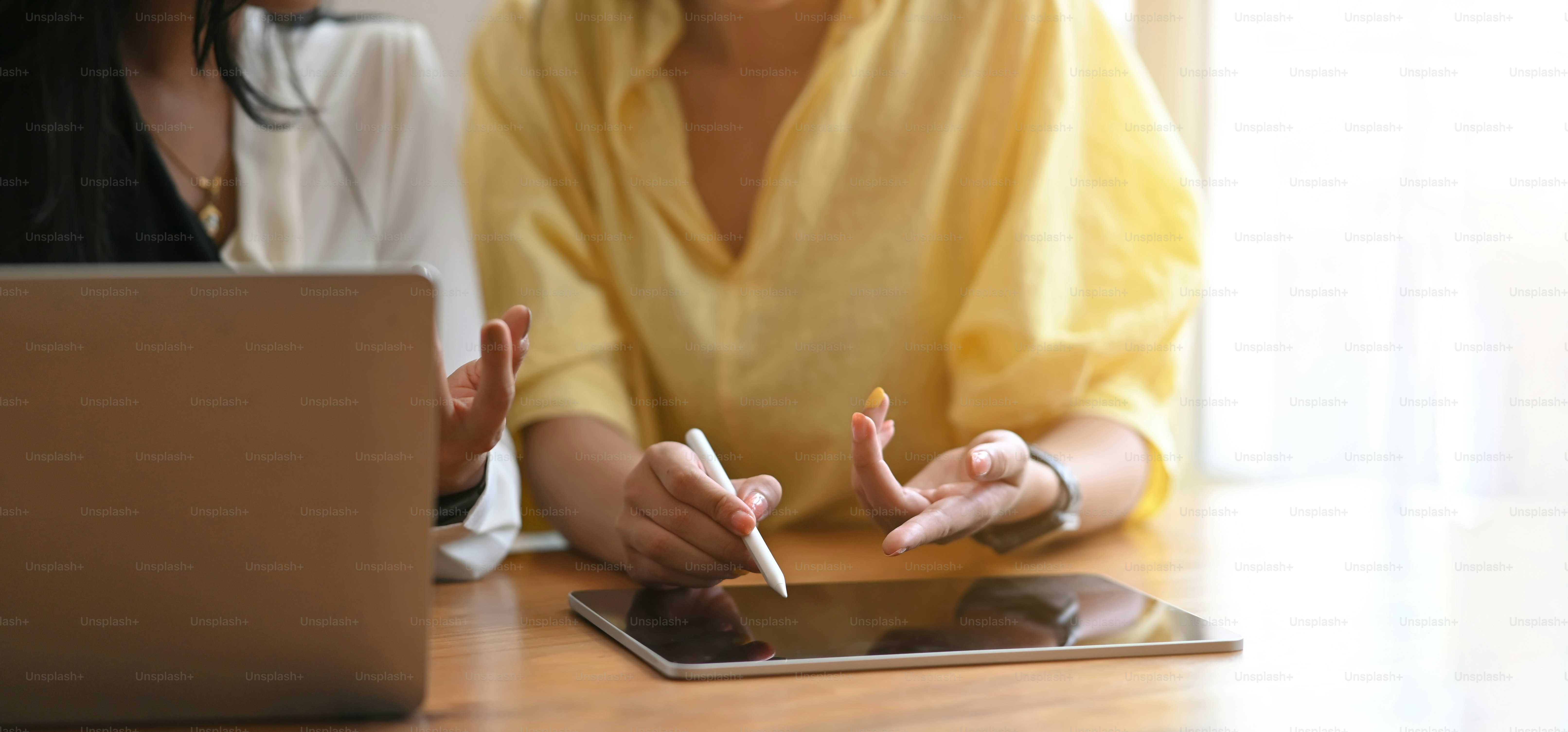 Businesswomen are working together by using a computer laptop and tablet at the wooden working desk.