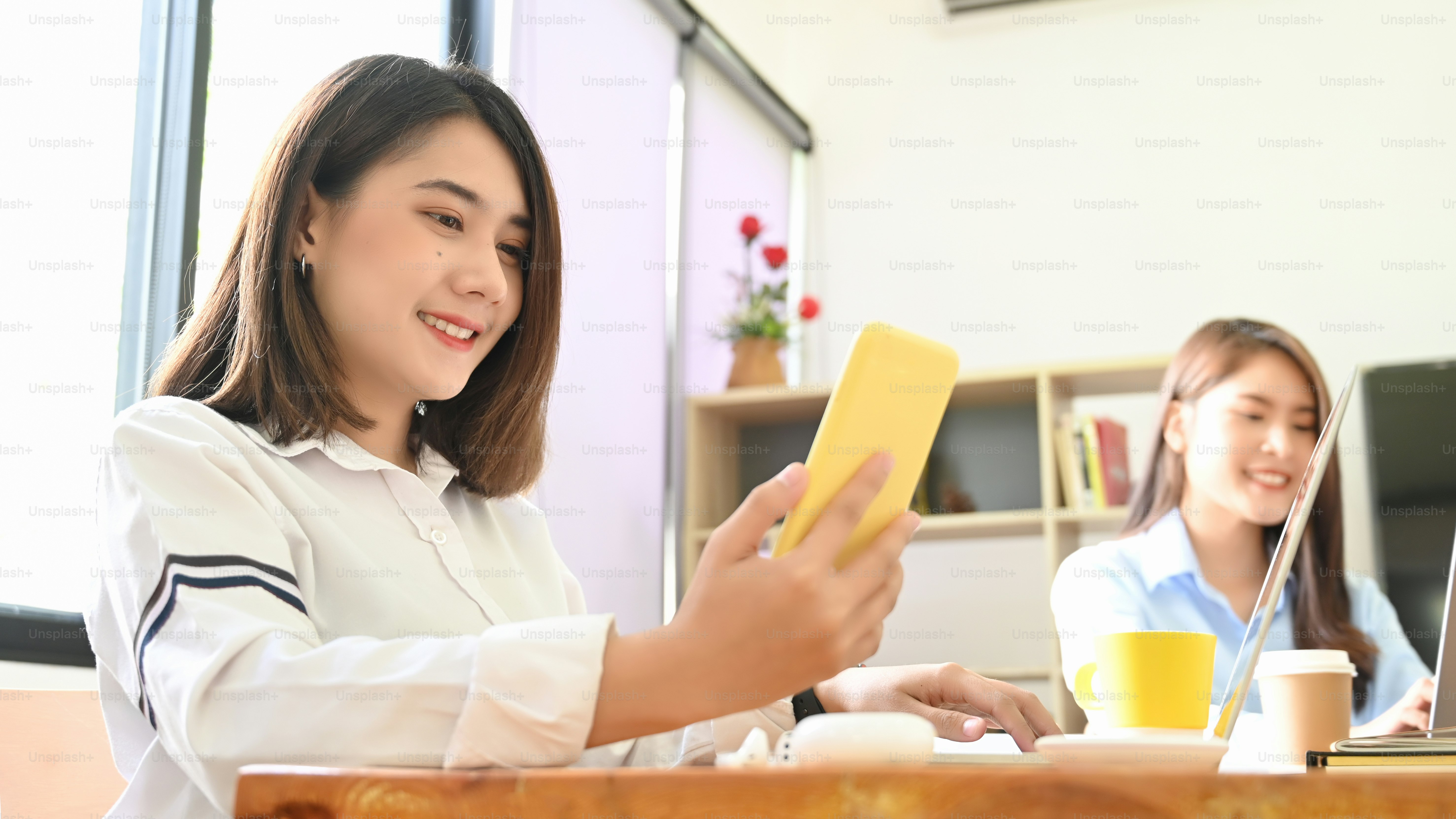 Seorang wanita menggunakan smartphone saat bekerja di meja kerja kayu.