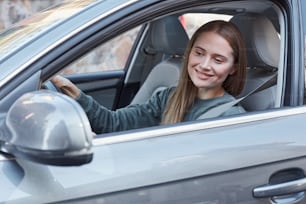 Positive attractive woman driving automobile while looking at rear view mirror