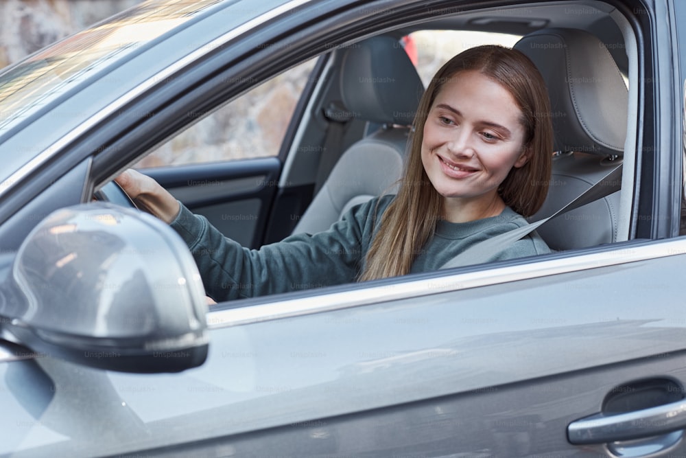 Donna attraente positiva che guida l'automobile mentre guarda lo specchietto retrovisore