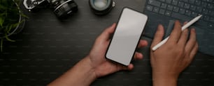 Top view of male holding mock-up smartphone and working on digital tablet on dark office desk