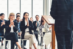 Group of business people meeting in a seminar conference . Audience listening to instructor in employee education training session . Office worker community summit forum with expert speaker .