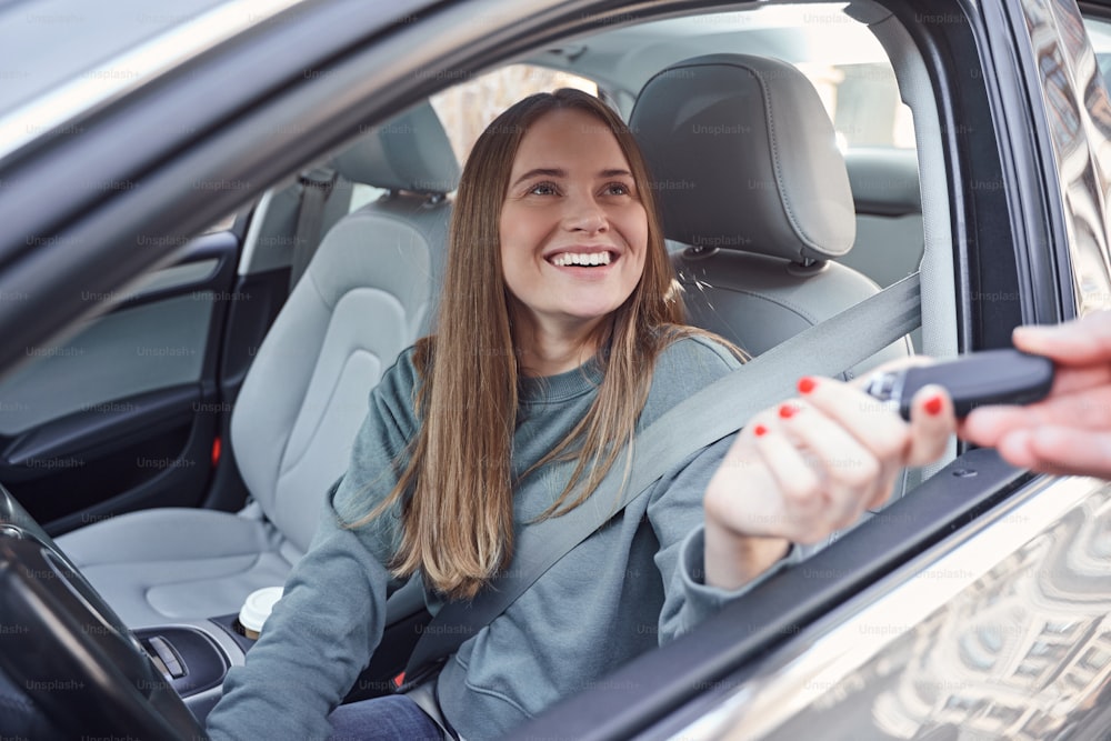 Allegra femmina che si sente soddisfatta mentre si siede in un'auto moderna e prende la chiave del telecomando