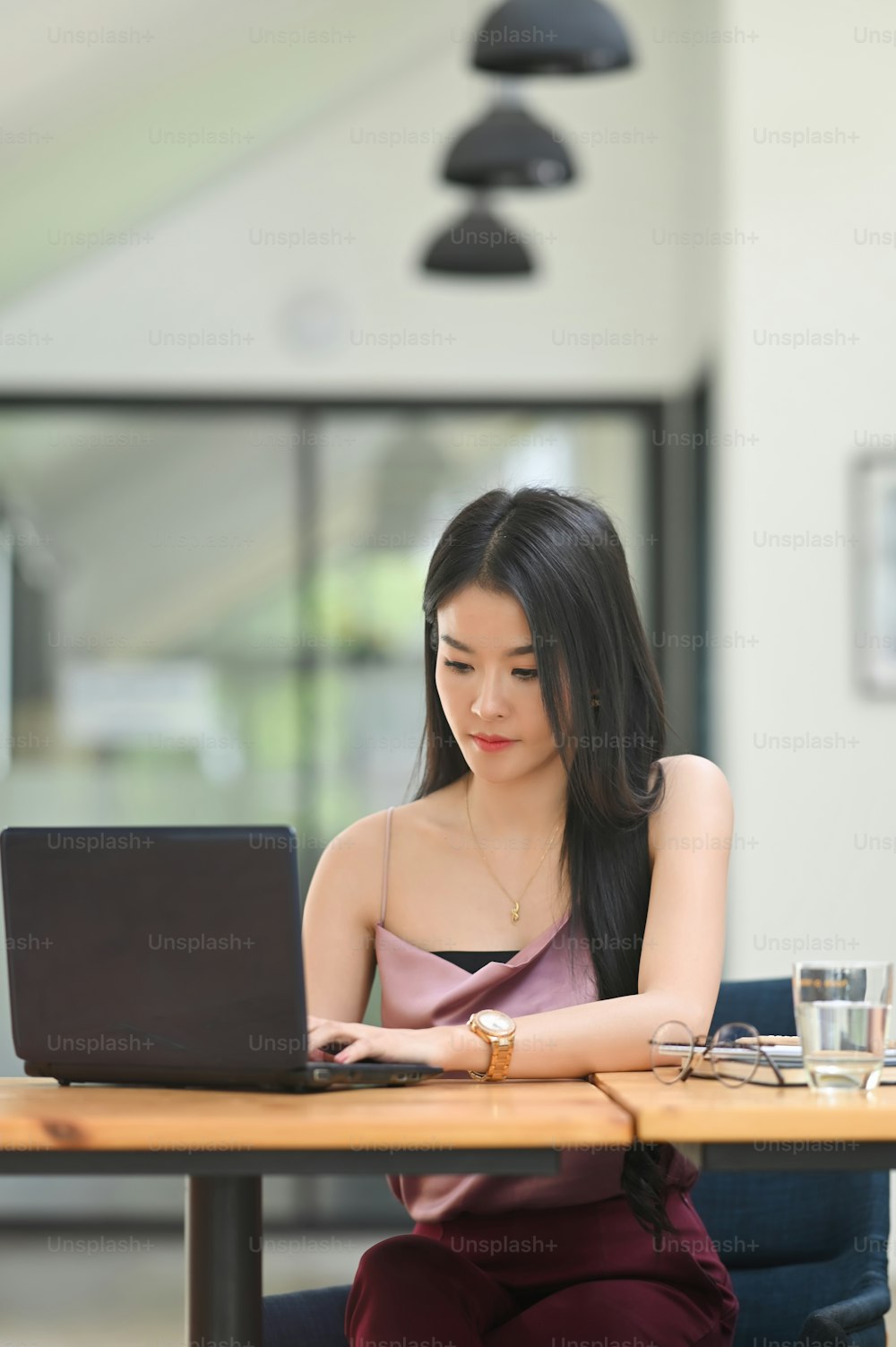Uma mulher está trabalhando com um laptop de computador enquanto está sentada na mesa de trabalho de madeira.