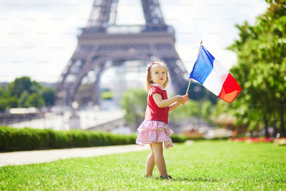 Bella bambina con bandiera tricolore nazionale francese vicino alla torre Eiffel a Parigi, Francia. 14 luglio (giorno della presa della Bastiglia), principale festa nazionale francese