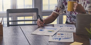 Cropped image of a woman is working with graphic charts while sitting at the white working desk.