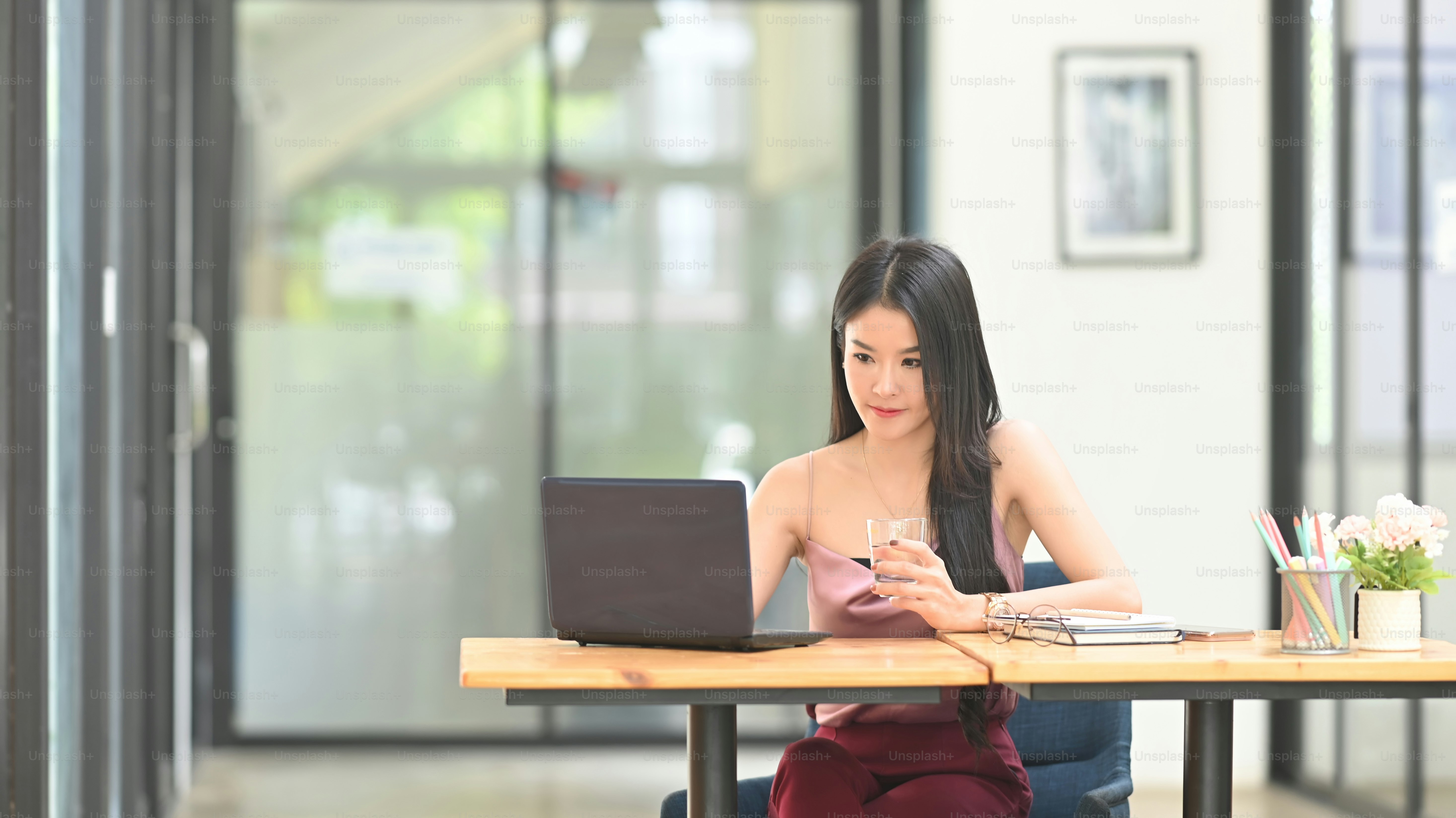 A beautiful Asian woman is sitting in front of a computer laptop at the wooden working desk.