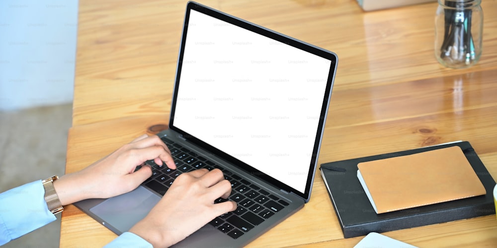 Cropped image of hands is using a white blank screen computer laptop at the wooden working desk.