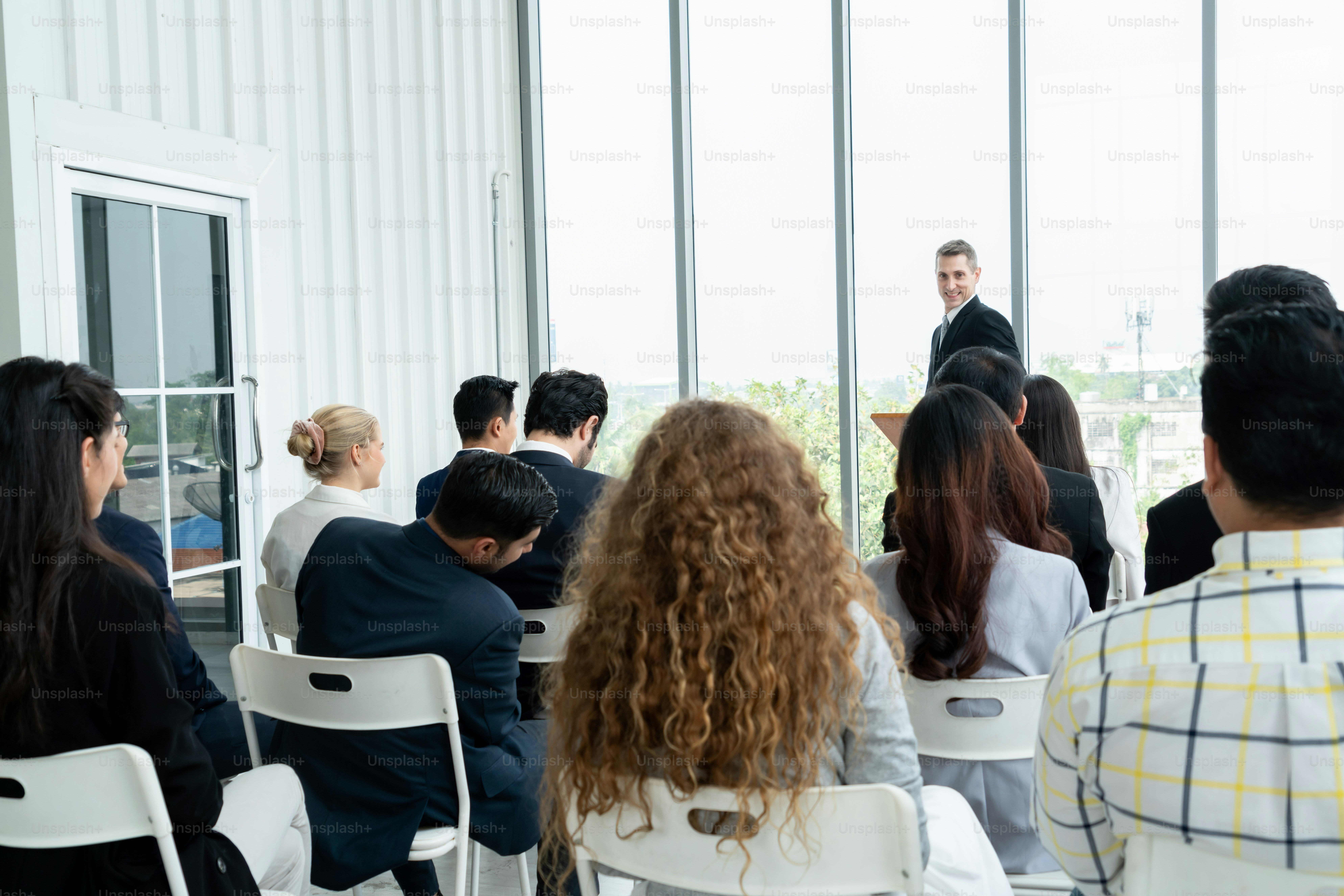 Group of business people meeting in a seminar conference . Audience listening to instructor in employee education training session . Office worker community summit forum with expert speaker .