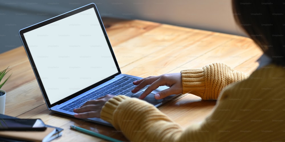 Cropped image of hands is using a white blank screen computer laptop at the wooden working desk.
