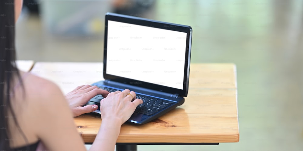 Atrás da foto da bela mulher está trabalhando com um laptop de computador de tela branca em branco na mesa de madeira.