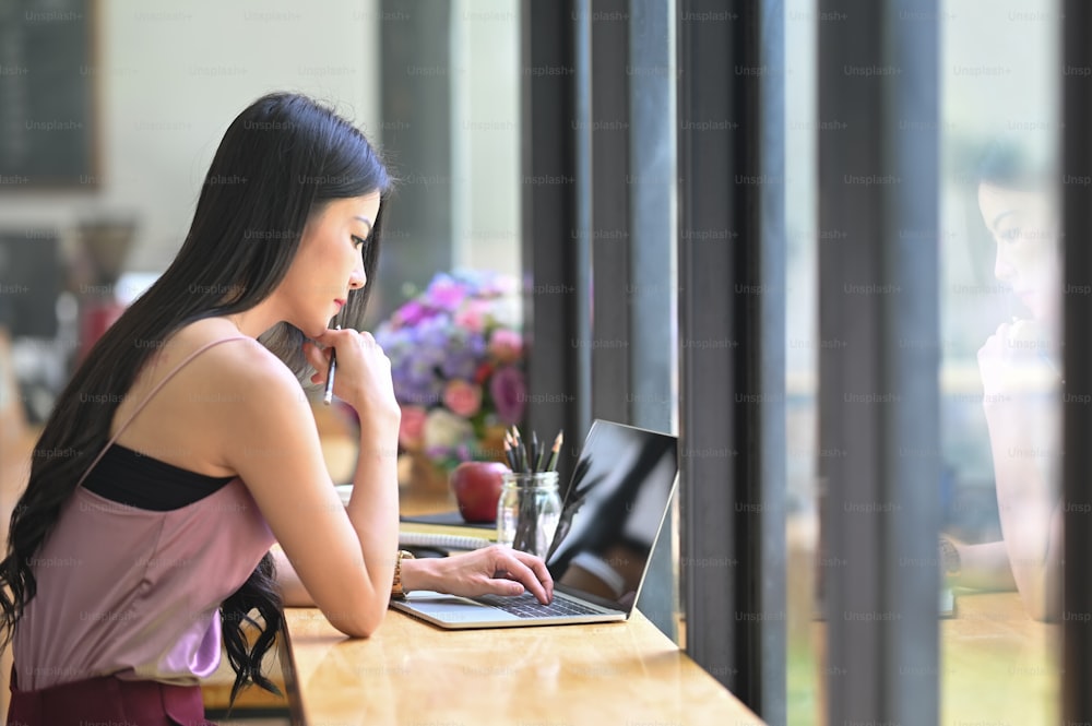 Una joven asiática está trabajando con una computadora portátil de pantalla negra en blanco en el mostrador de madera.