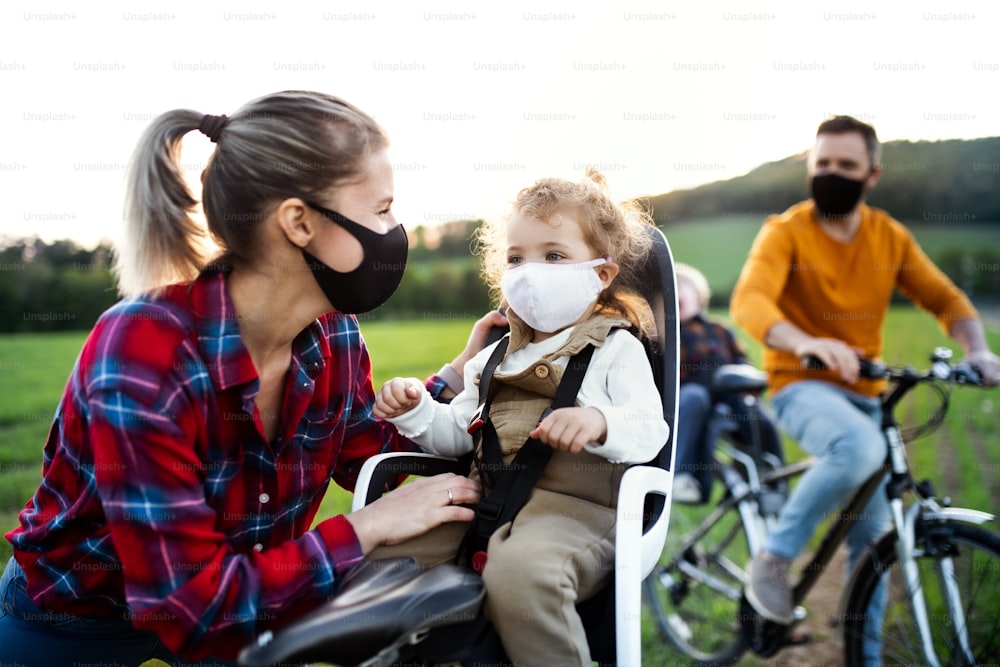 Famille avec deux jeunes enfants en voyage à vélo dans la nature, portant des masques faciaux.