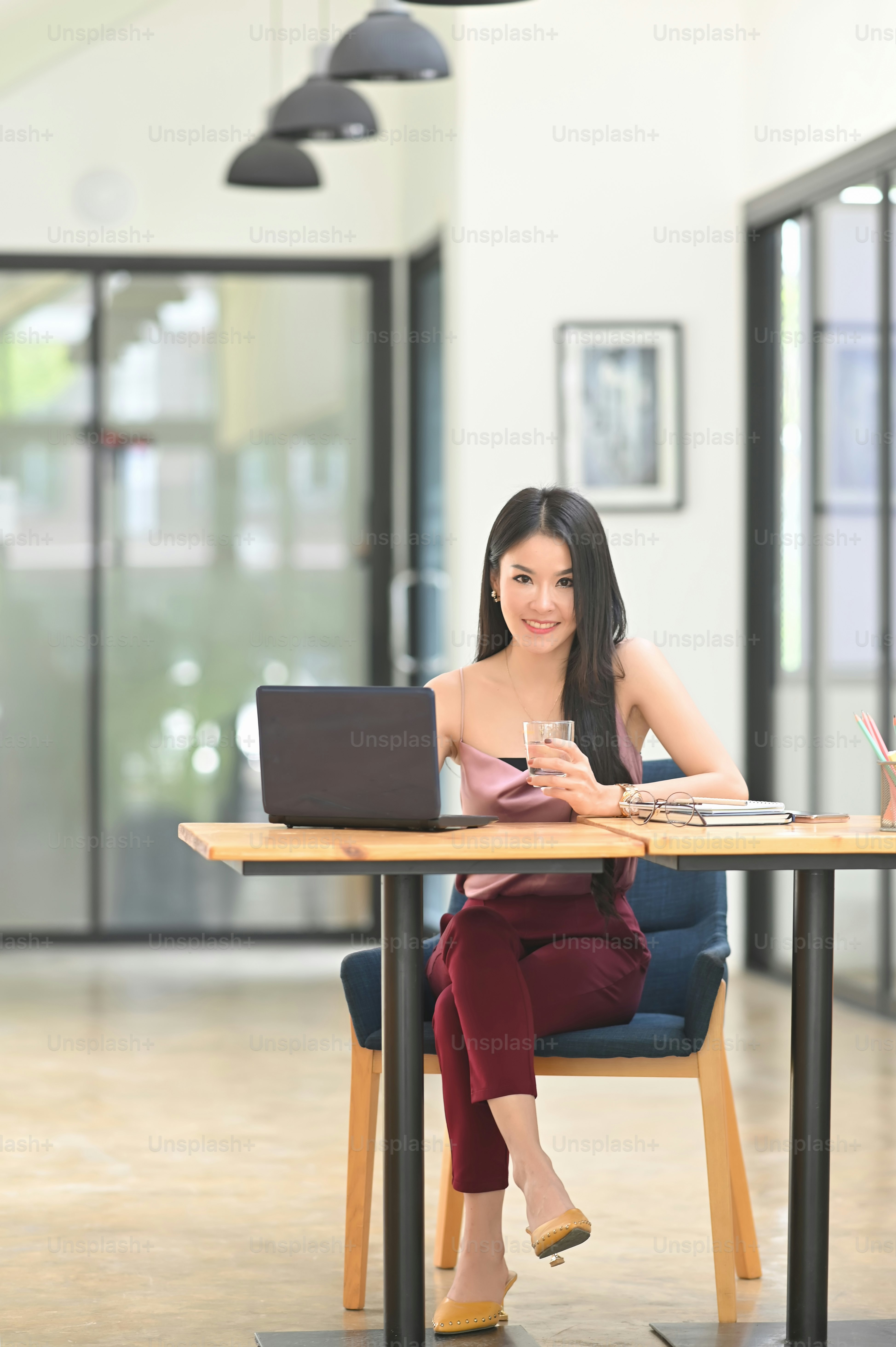 A beautiful Asian woman is sitting in front of a computer laptop at the wooden working desk.