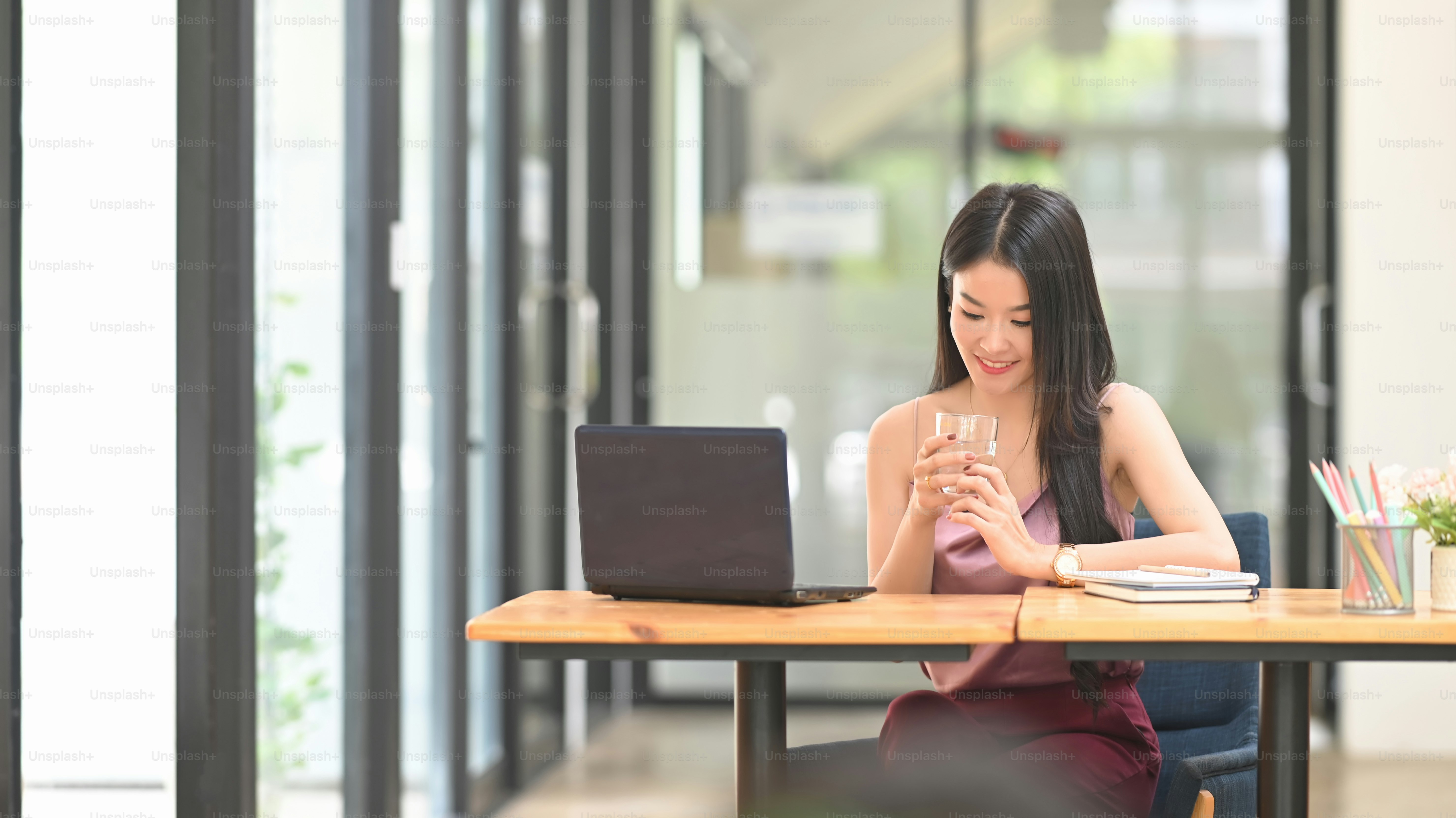 Young Asian woman is using a computer laptop while sitting at the wooden working desk.
