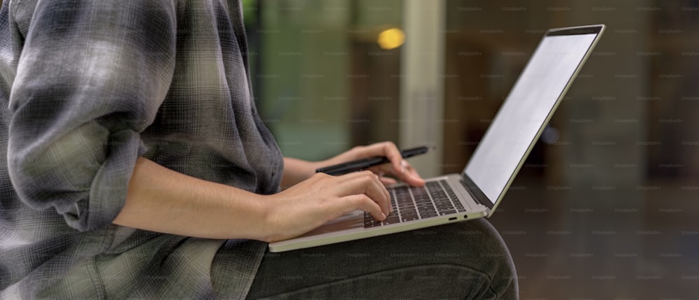 Vue latérale d’une travailleuse assise sur une table tout en travaillant avec une maquette d’ordinateur portable dans un bureau confortable