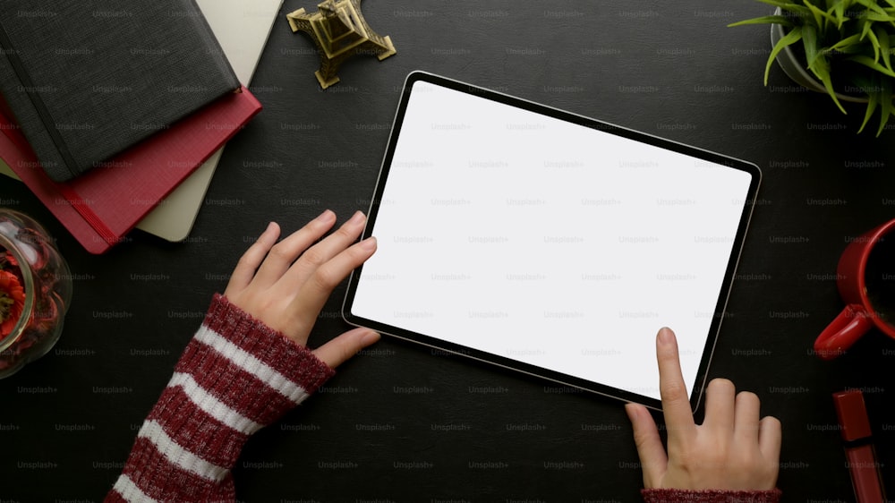 Overhead shot of female hand touching on mock-up digital tablet on  feminine stylish worktable with supplies and decorations
